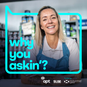 A photo of a person wearing a white polo shirt and green apron. They are leaning on a counter, looking at the camera with their arms folded and smiling. Behind them are tins of paint on shelves. Around them is a bright blue speech bubble with text that reads, why you askin'?